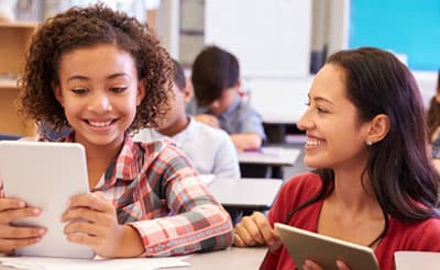 Girl writing on a tablet and getting help from the teacher